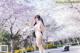 A woman in a white bikini standing in front of cherry blossoms.