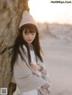 A woman leaning against a tree on the beach.