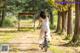 A woman in a white dress riding a bike in the woods.