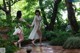 Two women in white dresses are walking through a garden.